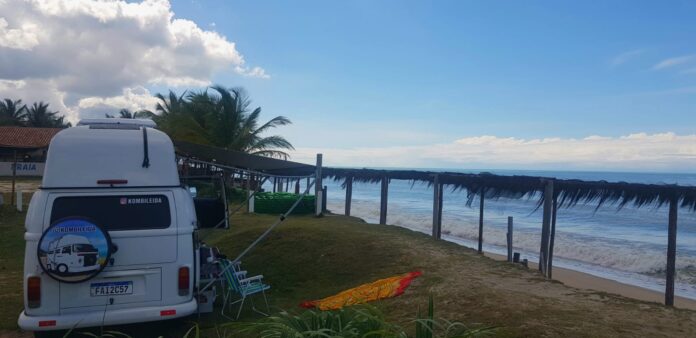 #paratodosverem Imagem mostra uma kombi-casa estacionada em frente ao mar.